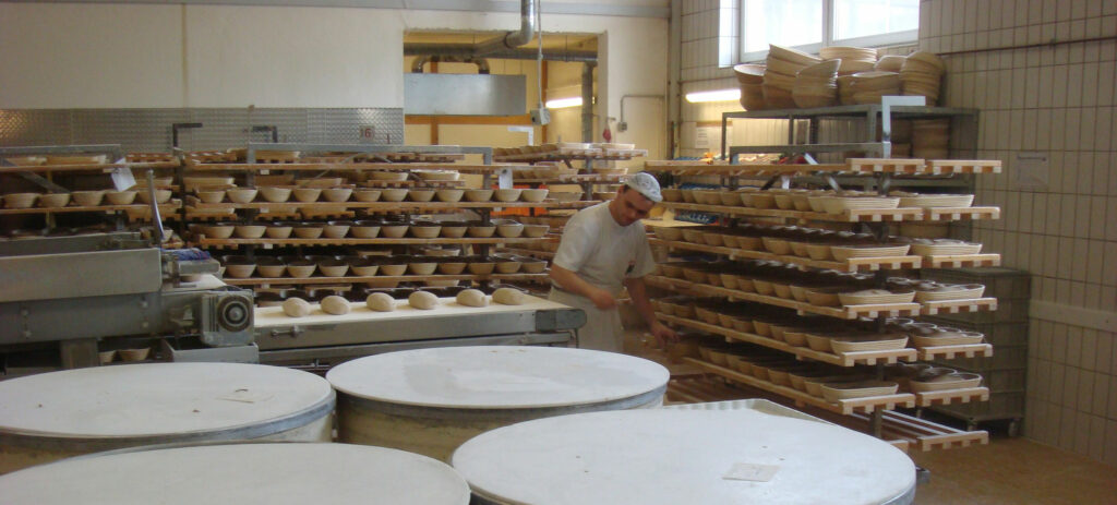 baker making bread in big bakery, rows of bread around